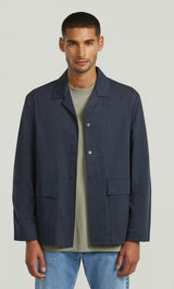 Man wearing a navy jacket over a green shirt on a light gray background