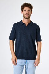 Man wearing a dark blue polo shirt and light blue jeans against a white background