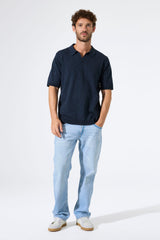 Man wearing a navy polo shirt and light blue jeans on a white background