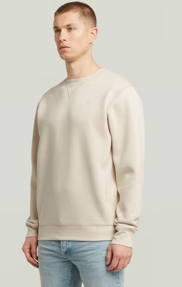 Man wearing a beige sweatshirt and light blue jeans against a plain background