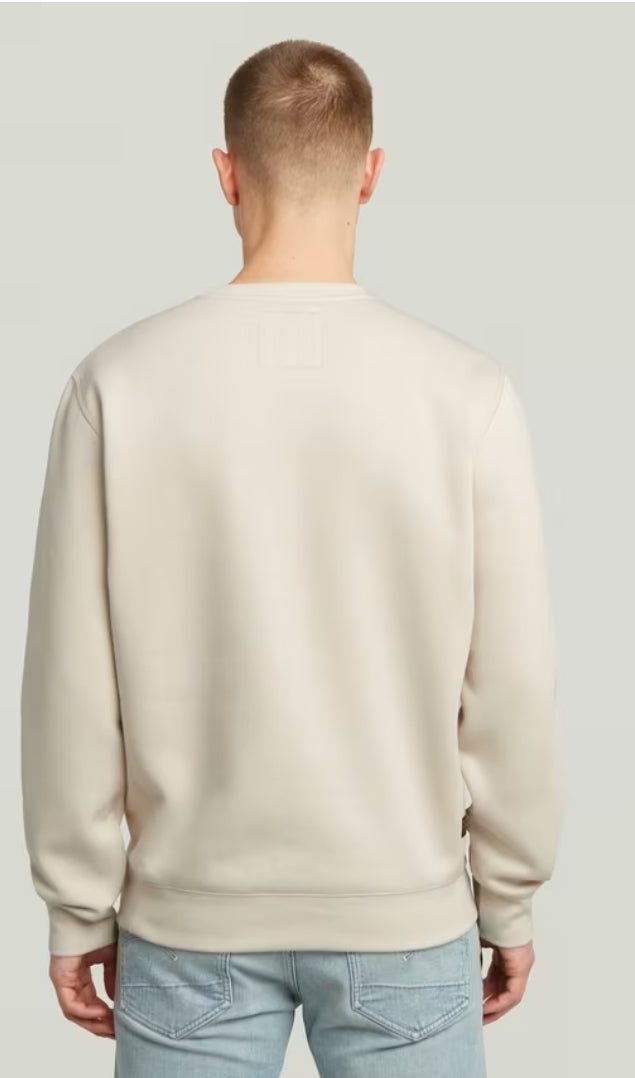 Man wearing a beige sweater and light blue jeans on a plain background