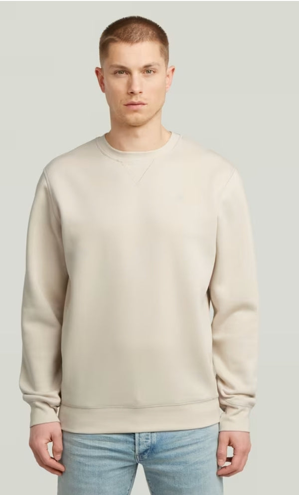 Man wearing a beige sweater and light blue jeans on a plain background