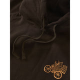 Close-up of a dark brown hoodie featuring a small embroidered gold owl in a cart on the lower right chest, with matching dark brown drawstrings visible.