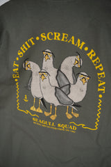 Close-up of a dark gray t-shirt featuring a yellow and white graphic of four seagulls with the text 'EAT • SHIT • SCREAM • REPEAT' and 'SEAGULL SQUAD'.