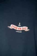 Close-up of a dark navy blue t-shirt featuring a vintage-style graphic with an anchor and a banner that reads 'FISH OR DIE' in red, with 'LAKOR' printed below in white.