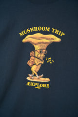 A close-up of a navy blue t-shirt featuring a yellow graphic of a mushroom character with sunglasses, a backpack, and musical notes, with the text 'MUSHROOM TRIP EXPLORE LAKEE' printed in yellow.
