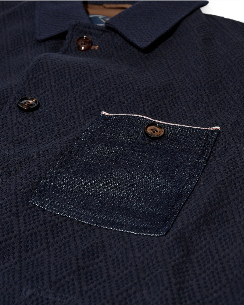 Close-up of a navy blue textured shirt with a pocket and buttons.