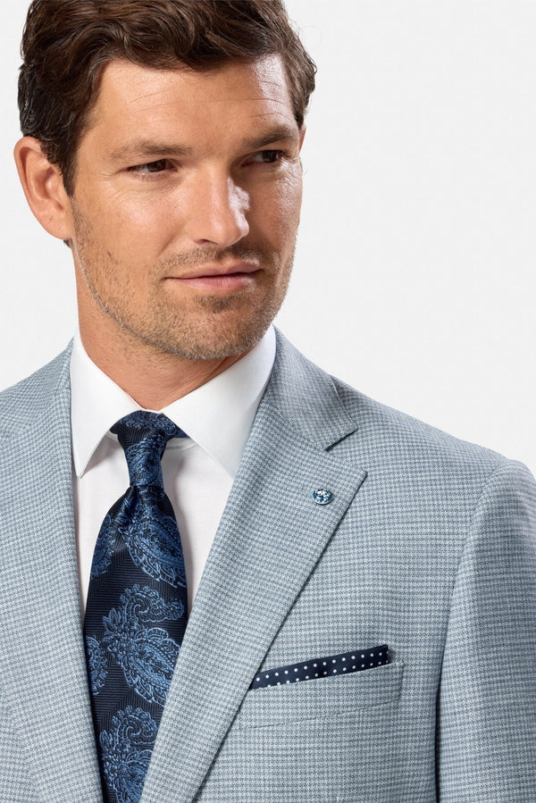 Man wearing a light blue suit with a blue patterned tie and pocket square on a white background