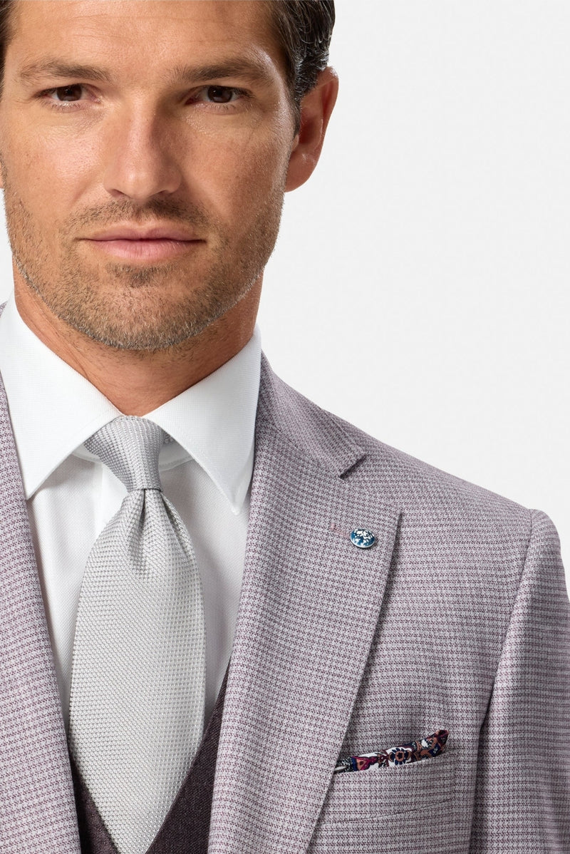 Man wearing a blush checkered suit with a white shirt and patterned tie on a light gray background