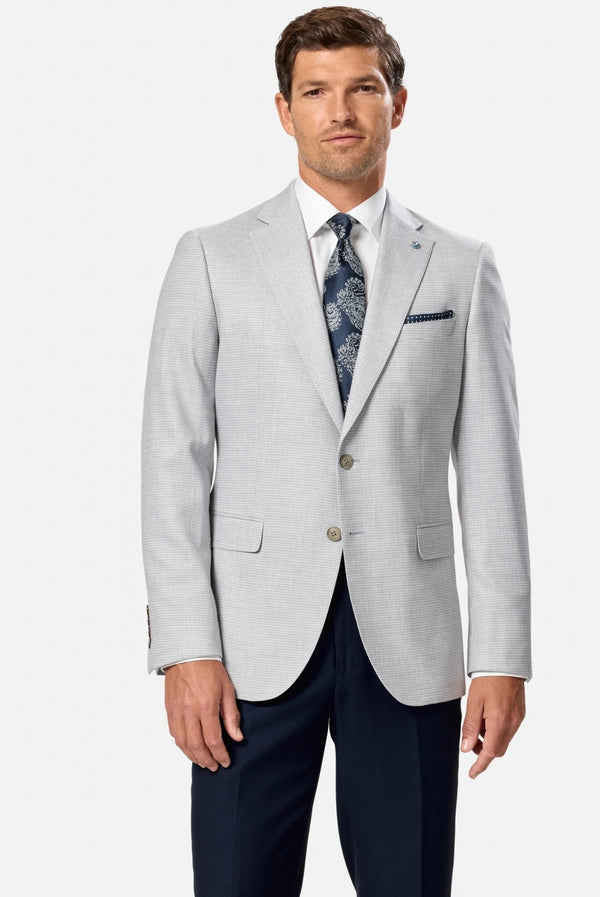 Man wearing a light gray blazer and dark blue pants with a patterned tie on a white background