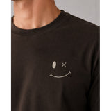 Close-up of a person wearing a dark brown crewneck sweatshirt with a white embroidered smiley face graphic on the chest.