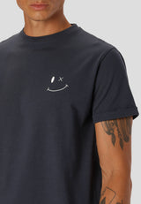 Person wearing a grey t-shirt with a white smiley face design on a plain background