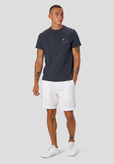 Man wearing a slate grey t-shirt and white shorts on a light gray background