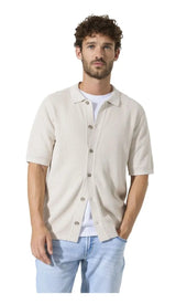 Man wearing a beige button-up shirt over a white t-shirt with light blue jeans on a white background