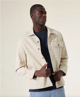 Man wearing a beige jacket over a dark shirt on a plain background