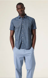 Man wearing a blue patterned shirt and light blue pants against a beige background