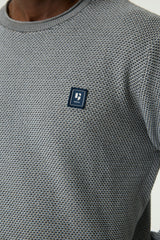 Close-up of a person wearing a textured navy crewneck sweater with a small dark chest logo patch.