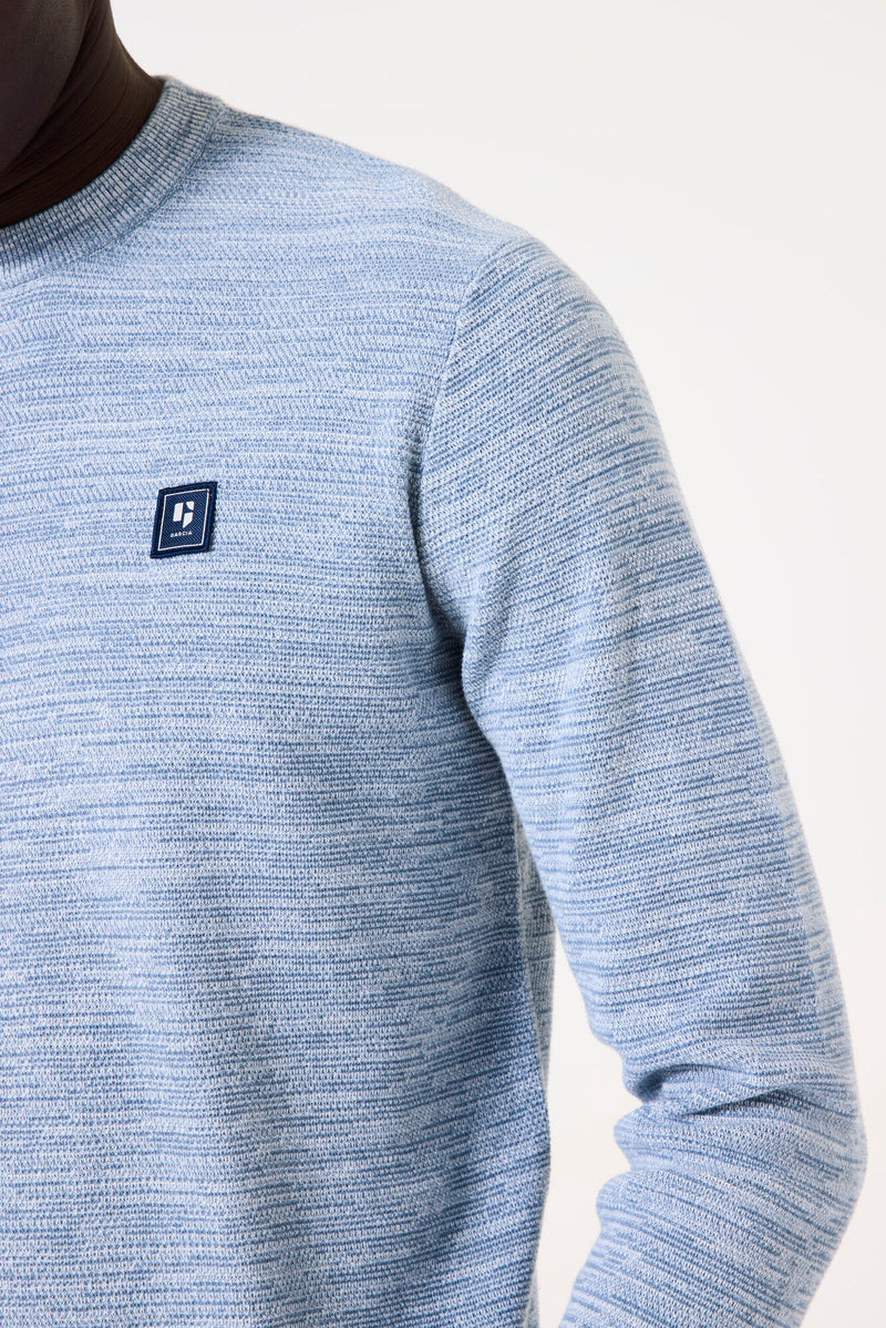 Close-up of a blue sweater with a brand logo on a white background