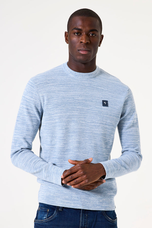 Man wearing a light blue sweater with a small logo on a white background