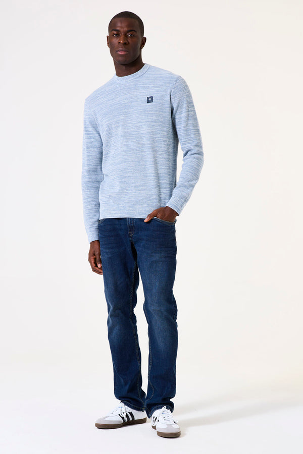 Man wearing a light blue sweater and dark blue jeans on a white background