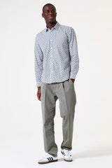 Man wearing a patterned shirt and gray pants with white sneakers on a white background