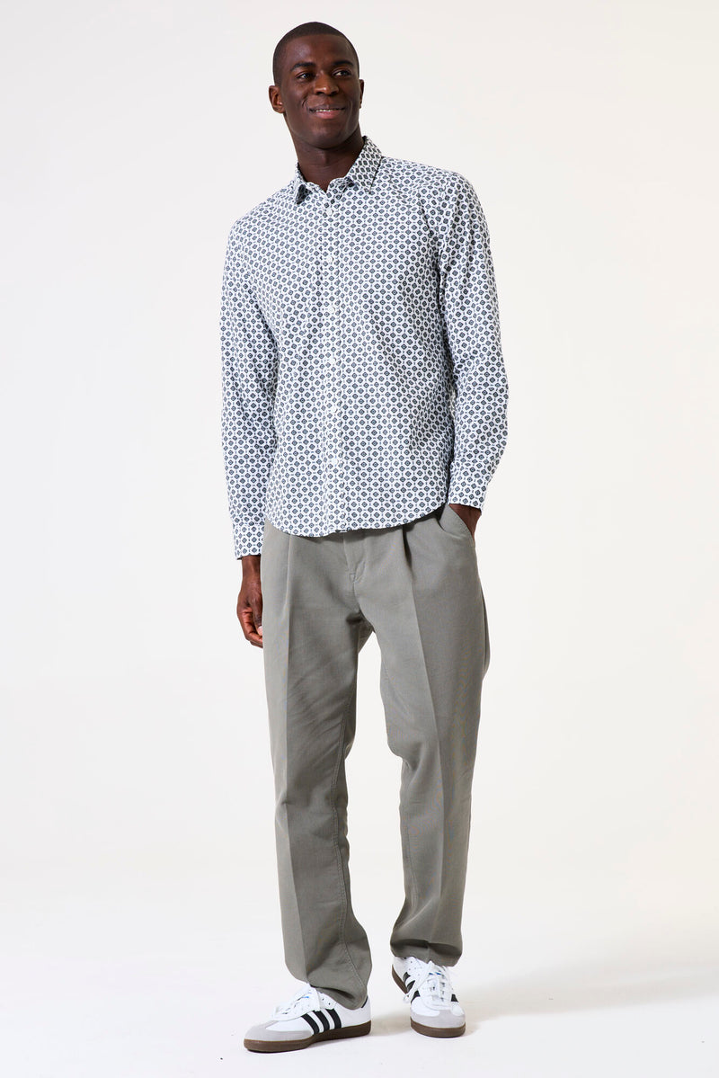 Man wearing a patterned shirt and gray pants with white sneakers on a white background
