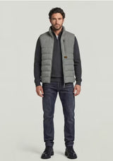 A man modeling a light gray puffer vest over a dark gray long-sleeve shirt, paired with dark blue jeans and black boots, against a solid light gray background.