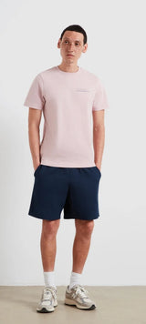 Man wearing a light pink t-shirt and navy shorts on a white background